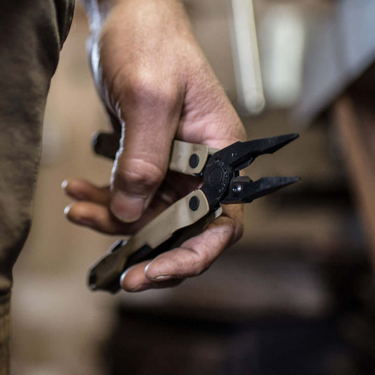 Close-up of a hand holding a Coyote Tan Leatherman Rebar® multitool with pliers, showcasing its rugged design.