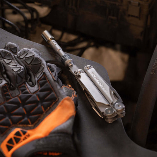 Stainless Steel Leatherman Wave® Plus multi-tool with ratchet driver beside protective gloves.