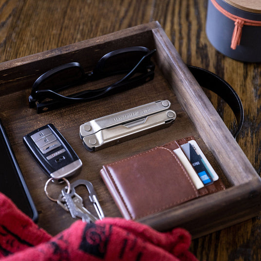 A stainless steel Leatherman Bond closed on a tray next to a wallet, keys and sunglasses.