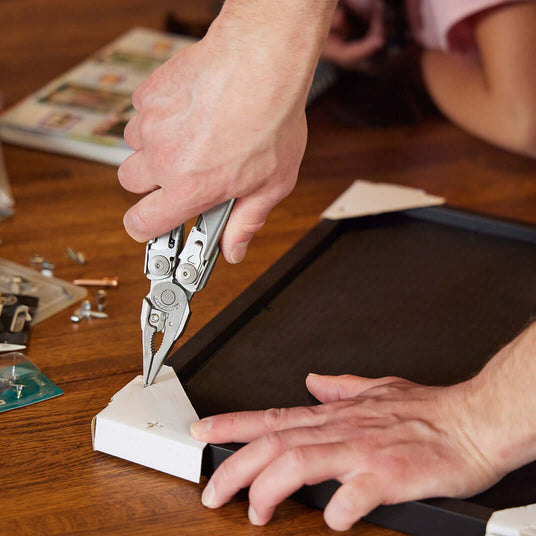 Someone using the pliers on a Leatherman Surge to fix a picture frame.