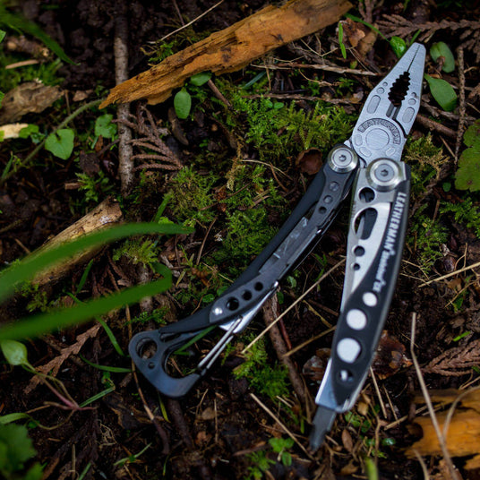 Black & Stainless Skeletool® CX multitool resting on mossy forest floor, showing its sleek design and versatility.