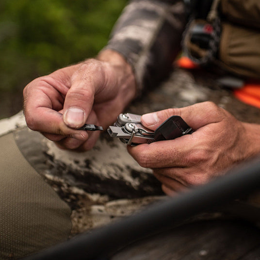 Person putting a bit on a Stainless Steel Leatherman Wave® Plus multitool in a natural setting.