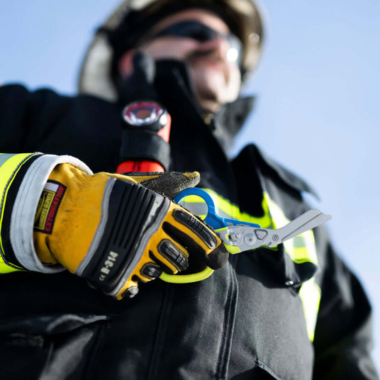 Firefighter holding a Yellow/Blue Leatherman Raptor® Rescue in a rescue-ready stance.