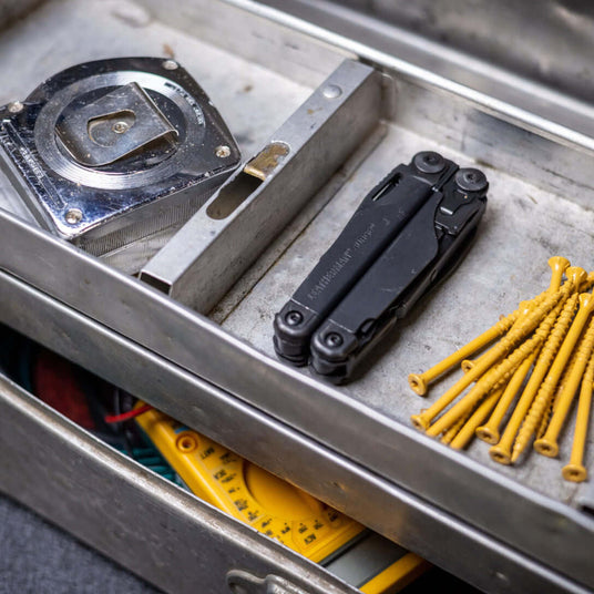 Black Leatherman Surge® multi-tool alongside measuring tape and screws in a toolbox.