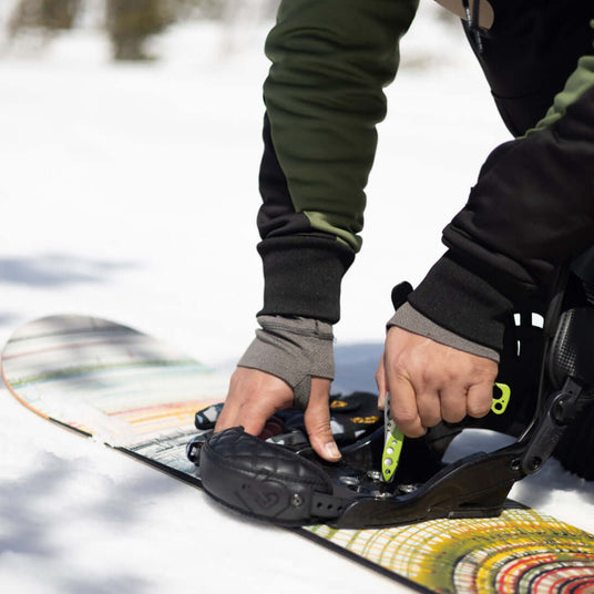 A snowboarding enthusiast using a Sublime Leatherman Skeletool® to adjust their snowboard bindings on the snowy mountain.