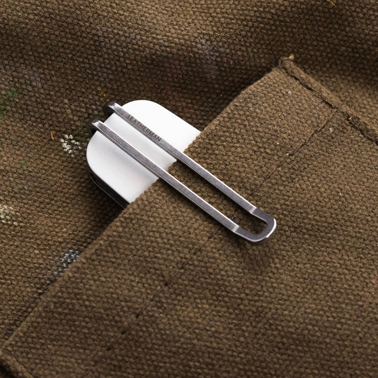 Translation missing: en.Leatherman Blazer Alpine folding knife clipped inside the pocket of a brown utility garment, with only the white handle and deep-carry pocket clip visible, highlighting convenient everyday carry