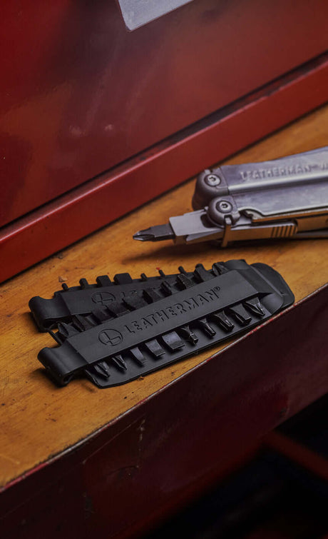 Leatherman Bit Kit Set laying on a wooden surface alongside a Leatherman Stainless Steel multi-tool with a bit attached.