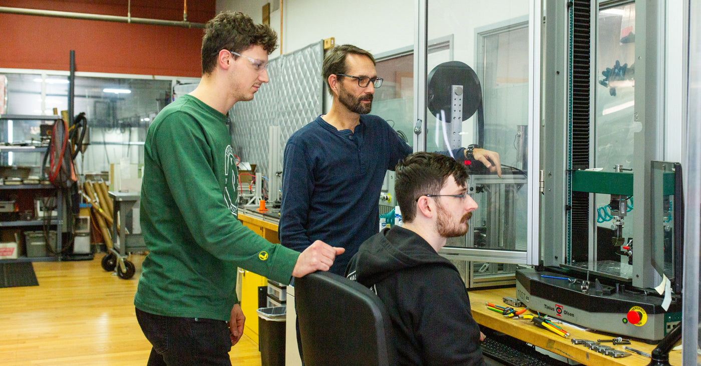 Translation missing: en.three men collaborating on a machine in a factory setting, focused on their task and surrounded by industrial equipment