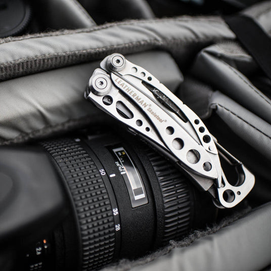 Stainless Steel Leatherman Skeletool® resting on top of a camera lens in a gear bag.