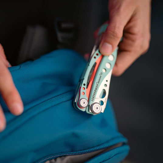 Person retrieving a Paradise Skeletool® CX multi-tool from a blue backpack, showcasing its compact design and functionality.