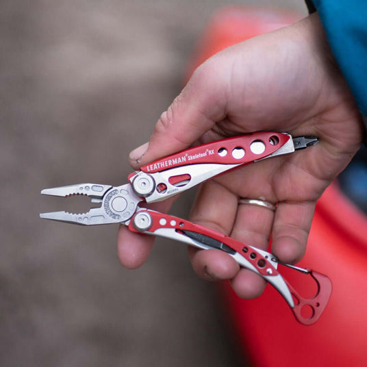 Hand holding a Red Leatherman Skeletool® RX multi-tool, showcasing its pliers and sleek red design.