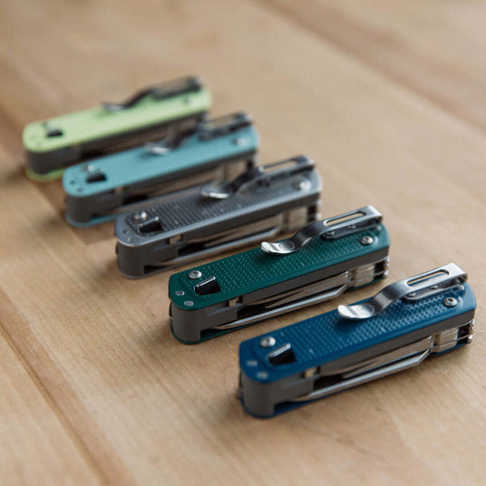 Collection of colorful FREE® T4 multitools arranged on a wooden surface, showcasing their sleek designs and features.