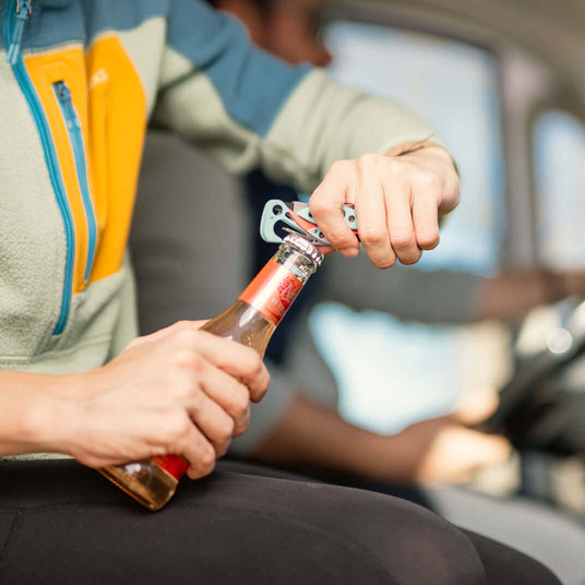 Translation missing: en.Person using the bottle opener on a Leatherman Skeletool CX in Paradise color to open a bottle