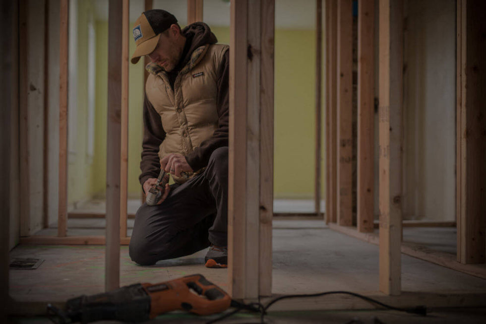 Translation missing: en.A man in a hat and jacket is actively engaged in work at a construction site, surrounded by tools and equipment