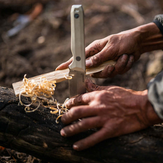 Person using an Alpine Leatherman Pioneer® knife to carve wood shavings outdoors.