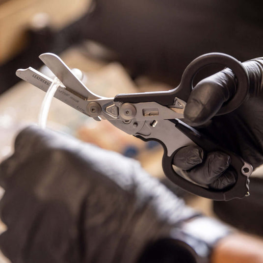 Close-up of a black Leatherman Raptor® Rescue tool in use, held by a gloved hand, showcasing its versatility.