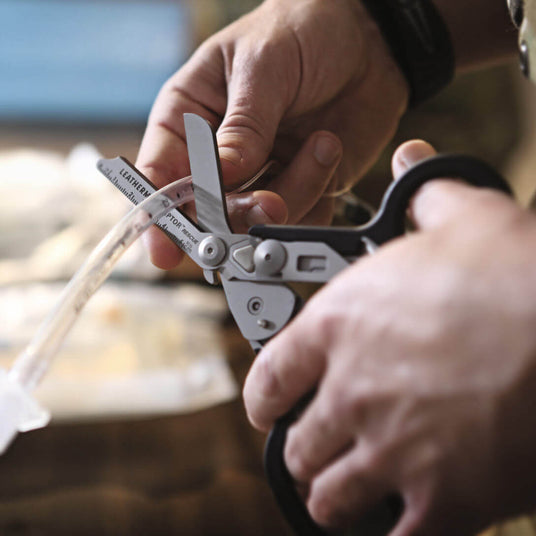 Close-up of hands using a Black Leatherman Raptor® Rescue shears on a medical tube for emergency situations.