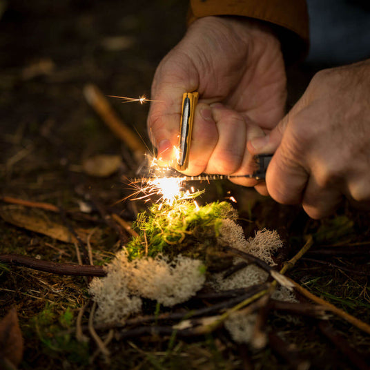 Hands using Leatherman Signal® to create sparks for fire starting in natural setting.