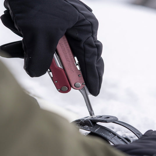 Translation missing: en.Person wearing black gloves using a Leatherman Rebar in Heathered Cranberry color to tighten gear outdoors on a snowy surface