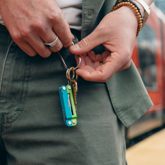 Translation missing: en.Person holding a Teal Twist Leatherman Micra® and keys while waiting at a train station, showcasing everyday carry essentials