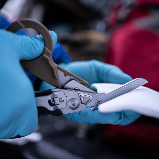 Translation missing: en.Hands in blue gloves using Coyote Black Raptor® Rescue shears to cut gauze