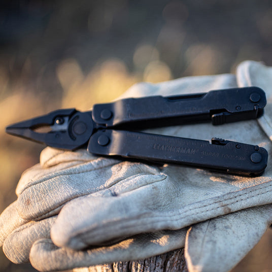 Translation missing: en.Leatherman Super Tool 300 multi-tool in black resting on beige gloves, showcasing its rugged design and functionality