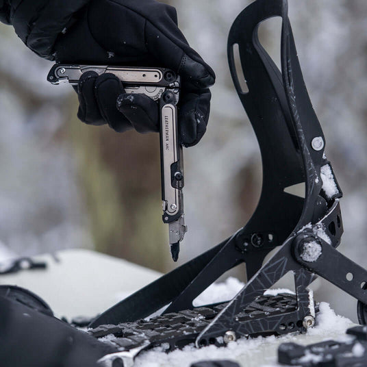Translation missing: en.Person using Black DLC & Stainless Steel Leatherman Arc® multitool while adjusting snowboard bindings in the snow