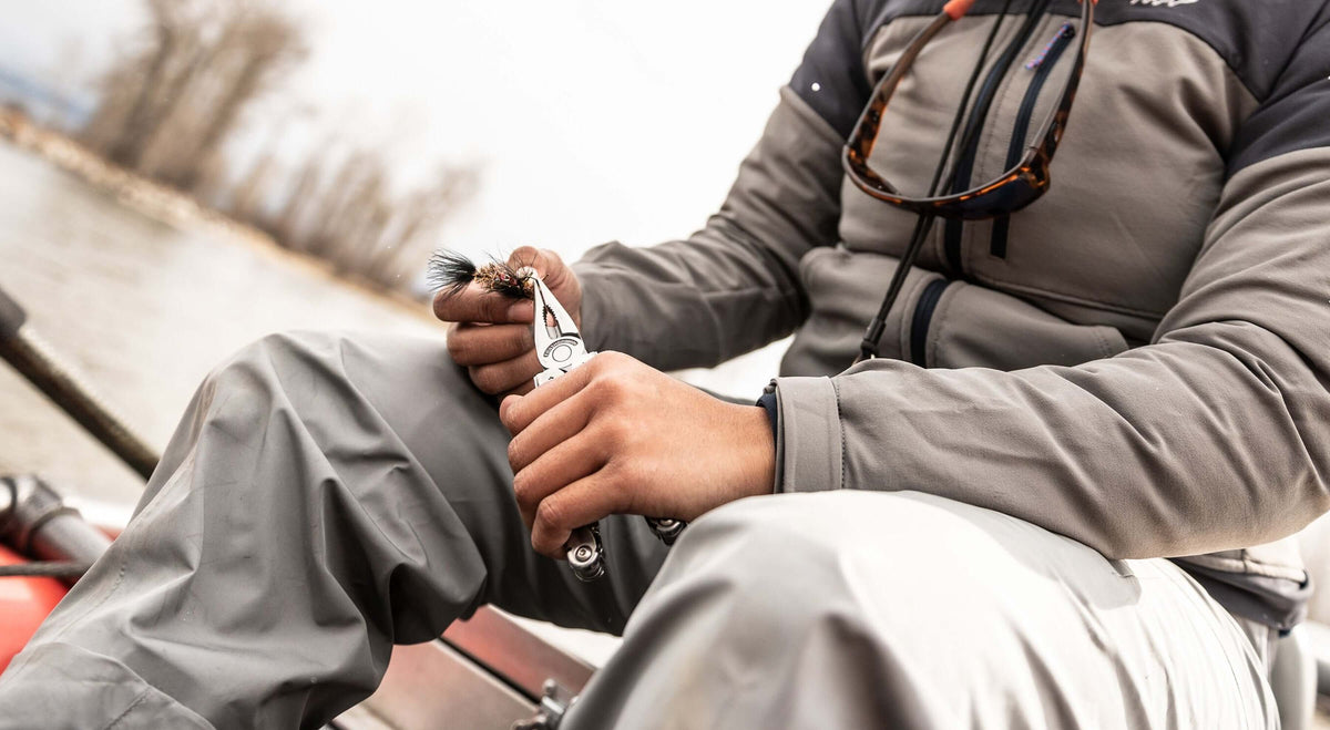Person using a stainless steel Leatherman multitool while fishing, showcasing its utility in outdoor settings.
