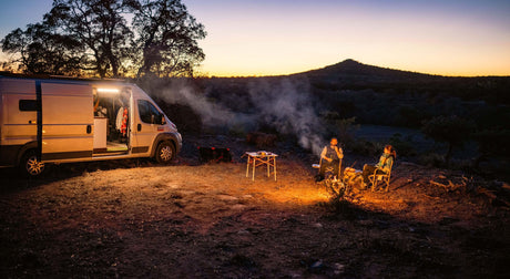 Translation missing: en.Campers enjoying a fire beside a van at sunset in a scenic outdoor location