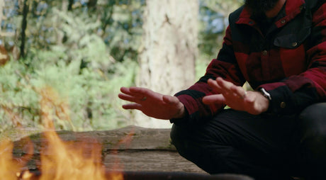 Man warming hands by a campfire in the forest.