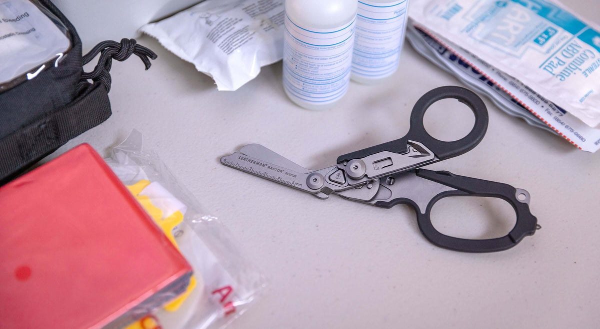 Black Leatherman Raptor® Rescue scissors on a table next to first aid supplies.