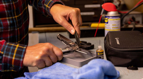 Translation missing: en.Person cleaning a stainless steel Leatherman Wave® Plus multitool on a workbench using the Leatherman Maintenance Kit