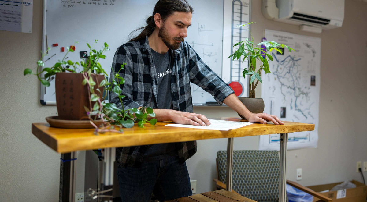 Seth Durham analyzing documents at a wooden table surrounded by plants in an office setting.