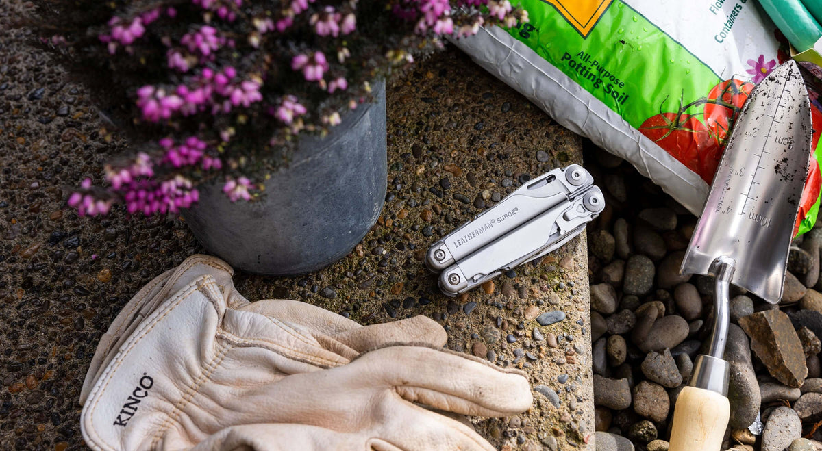 Stainless Steel Leatherman Surge® multi-tool beside gardening gloves and potting soil, perfect for outdoor projects.