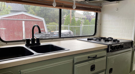 Translation missing: en.Modern RV kitchen with dual sinks, stove, and chic wooden countertop, with a view of an outdoor shed