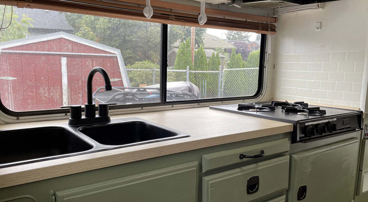 Modern RV kitchen with dual sinks, stove, and chic wooden countertop, with a view of an outdoor shed.