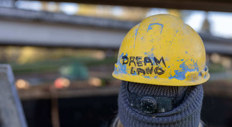 Translation missing: en.Close-up of a yellow hard hat with 'Dream Land' painted on it, set against a blurred construction background
