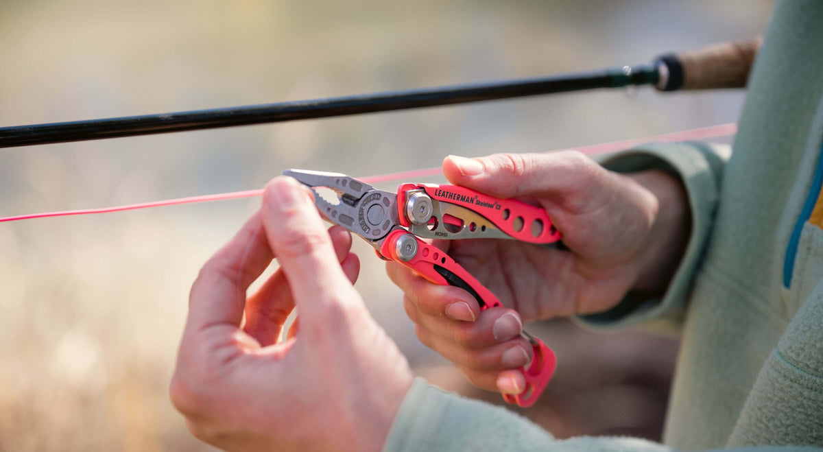 Close-up of a person using the Guava Leatherman Skeletool CX® while fishing, gripping fishing line with the tool.