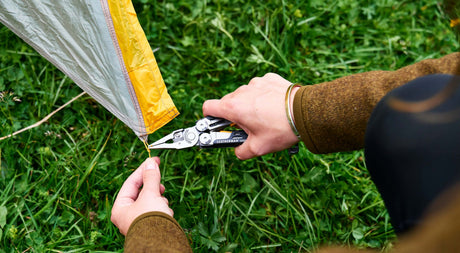 Person setting up a tent with a black and stainless Leatherman Signal.