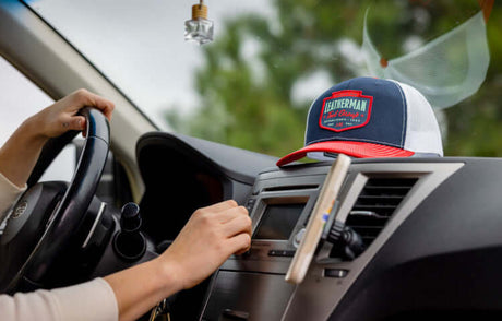 Translation missing: en.Navy and red Leatherman Pacific Northwest trucker hat on car dashboard with hand adjusting the stereo