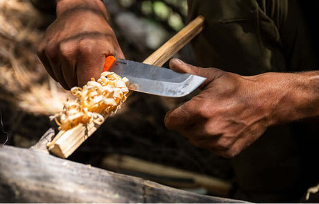 Translation missing: en.Close-up of hands using an Orange Pop Leatherman Pioneer™ knife to carve wood shavings outdoors
