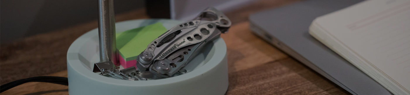 Translation missing: en.Stainless Steel Leatherman Skeletool® resting on a desk organizer beside a notebook and sticky notes in a modern workspace