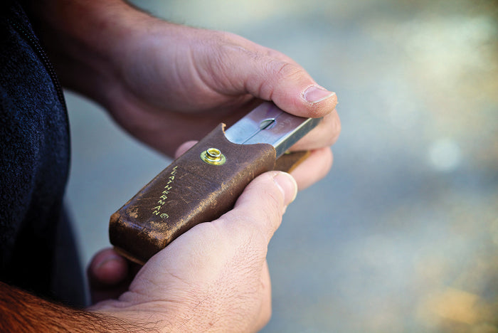 Translation missing: en.Someone holding a Leatherman PST partially in a brown leather sheath with a blurred natural background