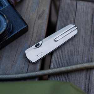 Translation missing: en.Leatherman Blazer Stainless Steel folding knife in closed position resting on a wooden surface beside a camera and outdoor gear, emphasizing everyday carry in an outdoor setting