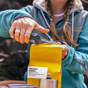 Translation missing: en.Person using the scissors on the Leatherman Wave® Alpha Cascadia multi-tool to open a bag of coffee beans outdoors