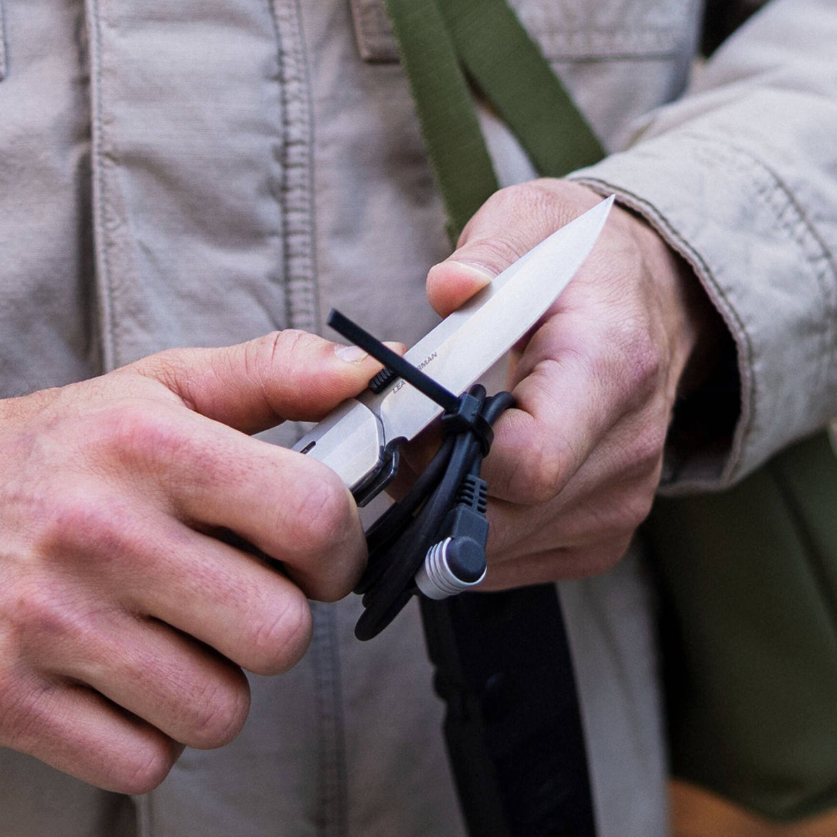 Translation missing: en.Person using a Leatherman Blazer Stainless Steel folding knife to cut a zip tie securing coiled cables, shown in a close-up with hands and utility jacket visible in an outdoor setting