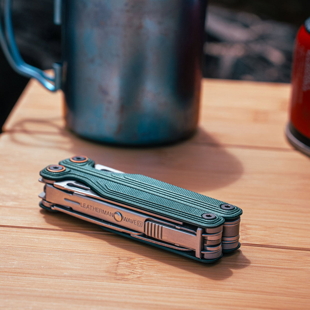 Translation missing: en.Leatherman Wave® Alpha Cascadia multi-tool folded and resting on a wooden camp table beside outdoor gear