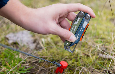 Translation missing: en.A person uses Leatherman Signal to hammer tent stake in patch of grass
