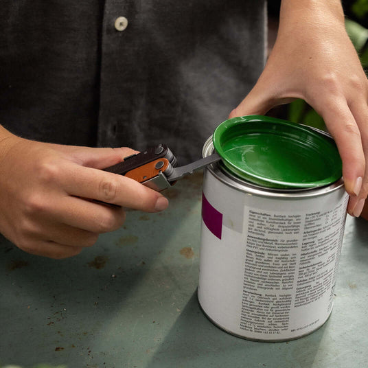 Translation missing: en.Person using the large screwdriver on a Leatherman Rebar in Burnt Sienna color to open a green-lidded paint can