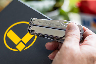 Translation missing: en.A Leatherman Wave+ is held by a person, displaying a distinctive logo on its handle